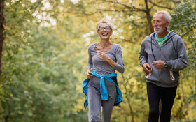 Aktives Seniorenpaar joggt gutgelaunt in einem Park.
