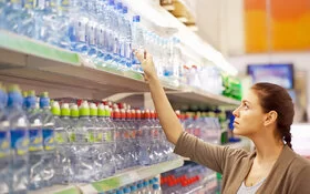 Eine Frau steht vor einem Getränkeregal mit Wasserflaschen in verschiedenen Verpackungen.