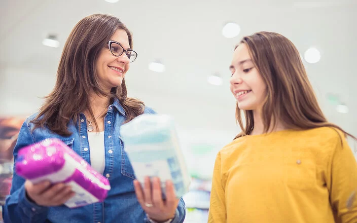 Eine Frau zeigt einem Mädchen verschiedene Menstruationsartikel im Einkaufsladen.