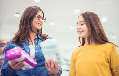 Eine Frau zeigt einem Mädchen verschiedene Menstruationsartikel im Einkaufsladen.