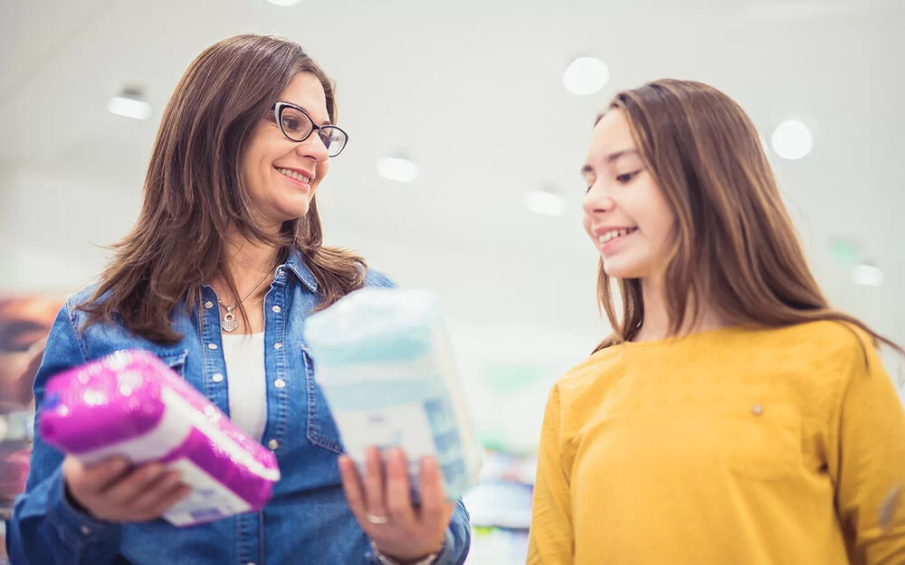 Eine Frau zeigt einem Mädchen verschiedene Menstruationsartikel im Einkaufsladen.