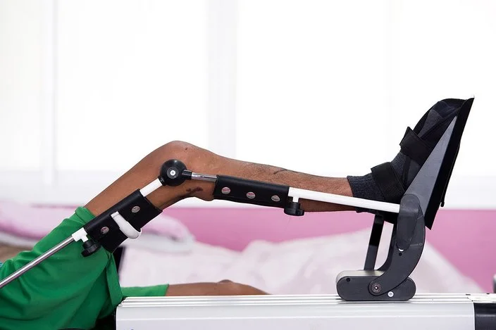 Eine Bewegungsschiene mobilisiert das Kniegelenk einer im Bett liegenden Person.