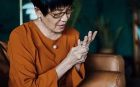 Eine ältere Frau reibt mit der einen Hand die Fingergrundgelenke der anderen.