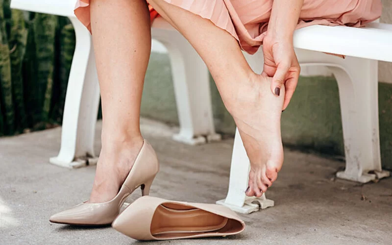 Eine Frau hat einen High-Heel-Schuh ausgezogen und hält sich den Fuß.