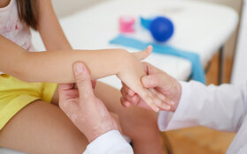 Ein Arzt untersucht den Arm und das Handgelenk eines Kindes wegen Verdacht auf Kinderheuma.