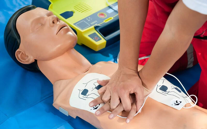 Eine Frau übt an einer Puppe die Wiederbelebung mit einem Defibrillator.