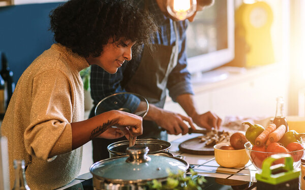 Eine Frau und ein Mann kochen gemeinsam in der Küche mit gesunden, frischen Zutaten, um einer Fettleber vorzubeugen.