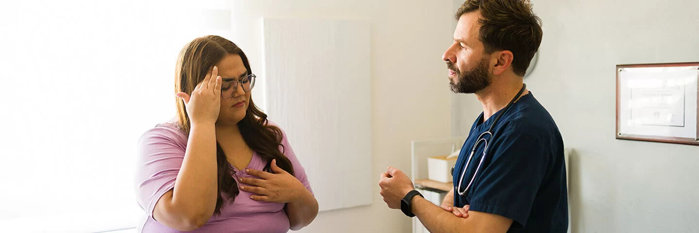 Eine Patientin mit Übergewicht sitzt im Behandlungszimmer auf einer Arztliege und spricht mit dem Arzt.