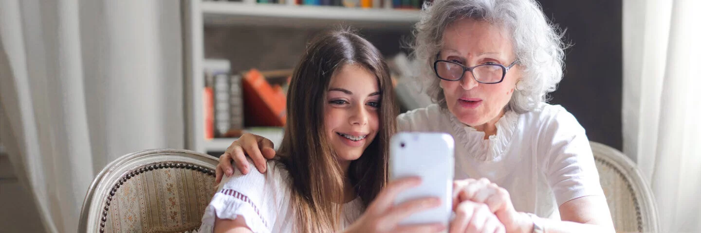 Eine Seniorin und ihre Enkelin schauen auf ein Smartphone.