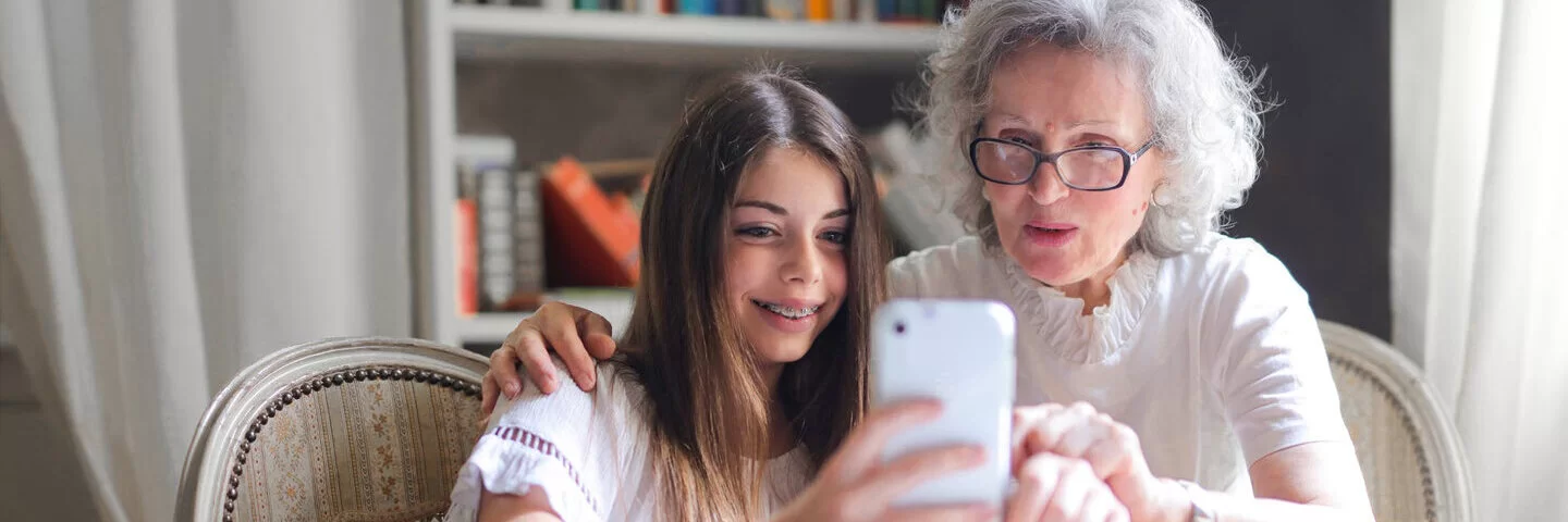 Eine Seniorin und ihre Enkelin schauen auf ein Smartphone.