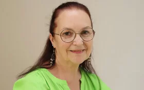 Claudia Missel trägt eine Brille und eine grüne Bluse und lächelt in die Kamera.