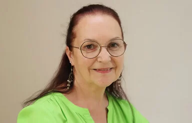 Claudia Missel trägt eine Brille und eine grüne Bluse und lächelt in die Kamera.
