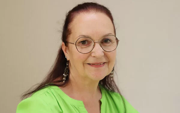 Claudia Missel trägt eine Brille und eine grüne Bluse und lächelt in die Kamera.