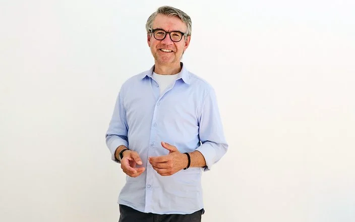 Der Psychologe Dr. Jürgen Theissing steht vor einer hellen Wand und lächelt in die Kamera.