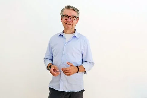 Der Psychologe Dr. Jürgen Theissing steht vor einer hellen Wand und lächelt in die Kamera.