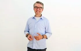 Der Psychologe Dr. Jürgen Theissing steht vor einer hellen Wand und lächelt in die Kamera.