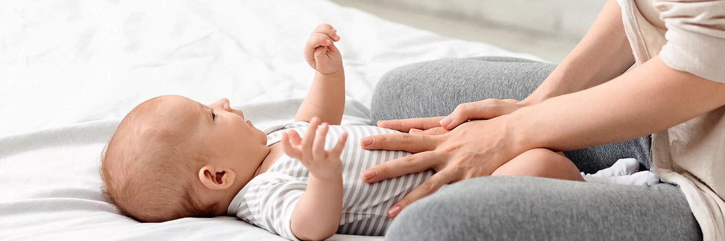 Eine Mutter massiert vorsichtig den Bauch ihres Babys, das an Blähungen leidet.