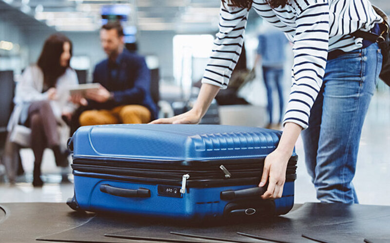 Eine Frau nimmt ihren Koffer vom Rollband in einer Flughafenhalle.