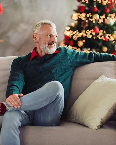 Ein älterer Mann sitzt Weihnachten alleine auf dem Sofa im Wohnzimmer.