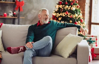 Ein älterer Mann sitzt Weihnachten alleine auf dem Sofa im Wohnzimmer.