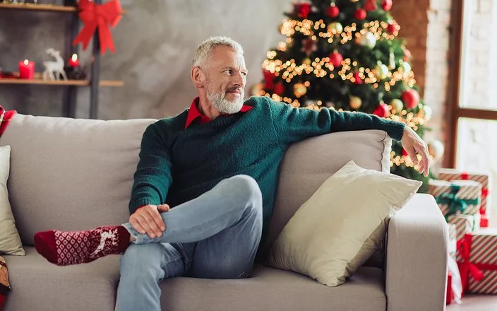 Ein älterer Mann sitzt Weihnachten alleine auf dem Sofa im Wohnzimmer.