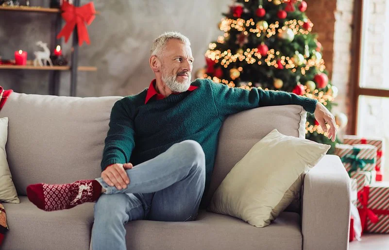 Ein älterer Mann sitzt Weihnachten alleine auf dem Sofa im Wohnzimmer.