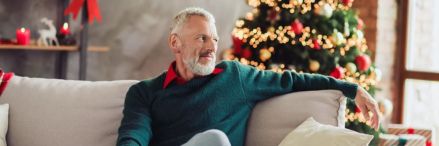 Ein älterer Mann sitzt Weihnachten alleine auf dem Sofa im Wohnzimmer.