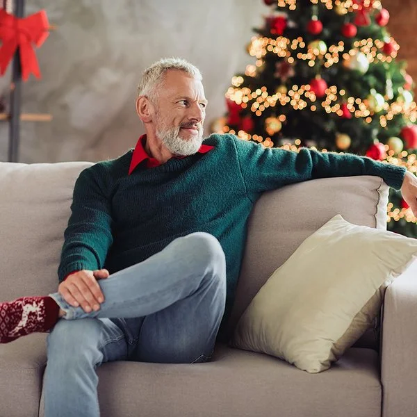 Ein älterer Mann sitzt Weihnachten alleine auf dem Sofa im Wohnzimmer.