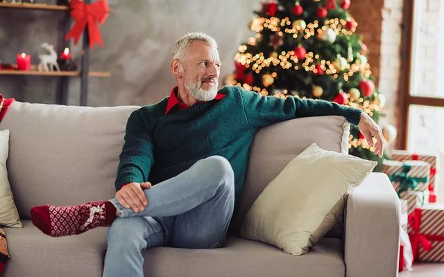 Ein älterer Mann sitzt Weihnachten alleine auf dem Sofa im Wohnzimmer.