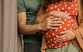 Eine schwangere Frau hält ihren Bauch, ihr Partner stützt sie. 