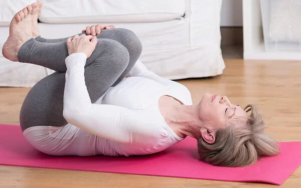 Frau mit Spinalkanalstenose macht Rückenübungen auf einer Yogamatte.