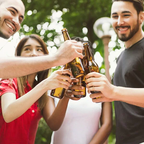 Fünf junge Leute stoßen im Garten mit Bierflaschen an. Die Gesichter sind angeschnitten und nicht zu erkennen.