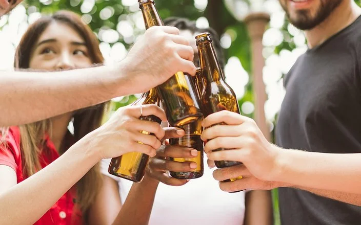 Fünf junge Leute stoßen im Garten mit Bierflaschen an. Die Gesichter sind angeschnitten und nicht zu erkennen.