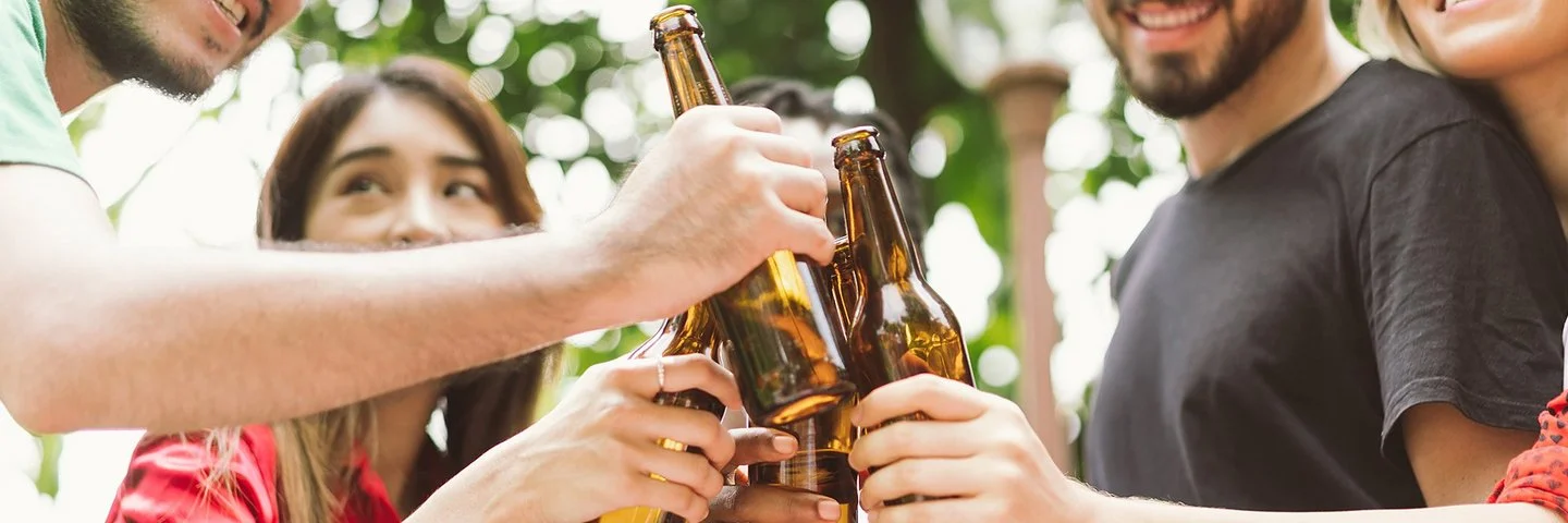 Fünf junge Leute stoßen im Garten mit Bierflaschen an. Die Gesichter sind angeschnitten und nicht zu erkennen.