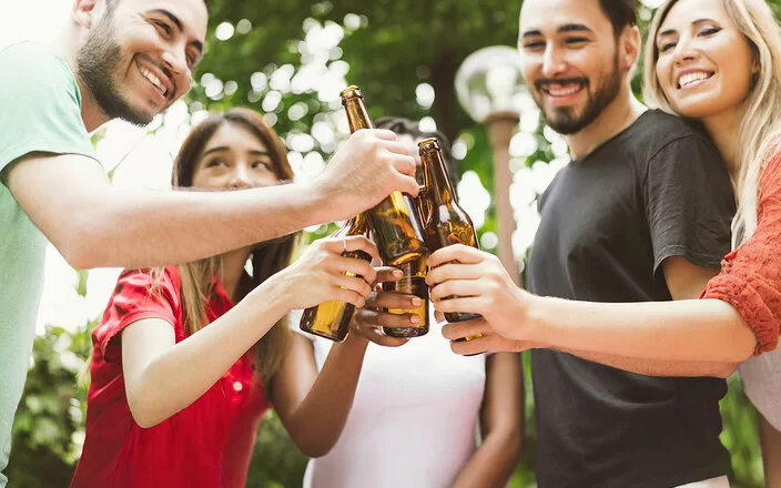 Fünf junge Leute stoßen im Garten mit Bierflaschen an. Die Gesichter sind angeschnitten und nicht zu erkennen.