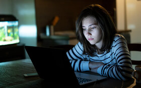Ein Mädchen sitzt im Dunklem am Laptop und ist traurig. Sie leidet unter Cybermobbing.