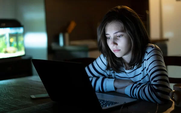 Ein Mädchen sitzt im Dunklem am Laptop und ist traurig. Sie leidet unter Cybermobbing.