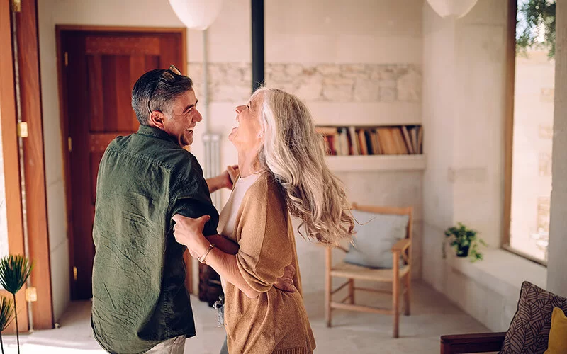 Ein Mann und eine Frau im mittleren Alter tanzen fröhlich in ihrem Haus.