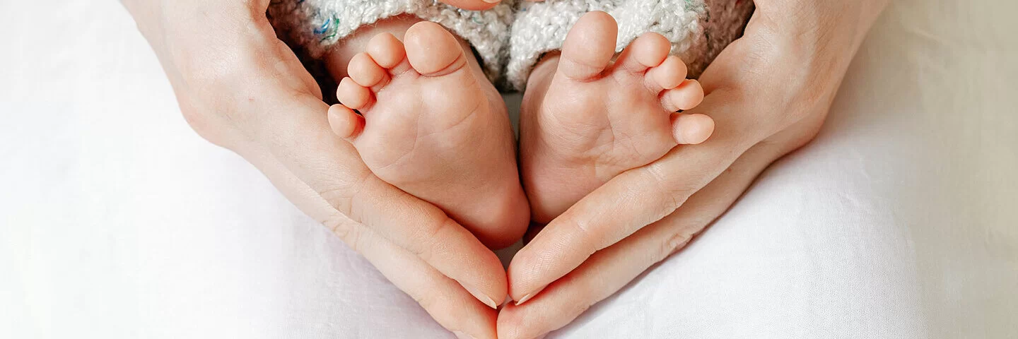 Winzige Babyfüße werden von Mutterhänden gehalten, die zu einem Herz geformt sind.