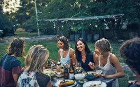 Eine Gruppe fröhlicher Personen sitzt an einem Gartentisch und genießt gesund Gegrilltes.