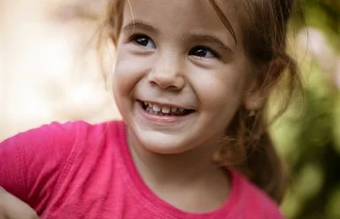 Ein ungefähr vierjähriges Mädchen schaut lächelnd zur Seite. Man sieht ihre gesunden Milchzähne.