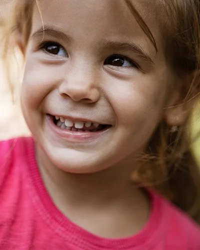 Ein ungefähr vierjähriges Mädchen schaut lächelnd zur Seite. Man sieht ihre gesunden Milchzähne.