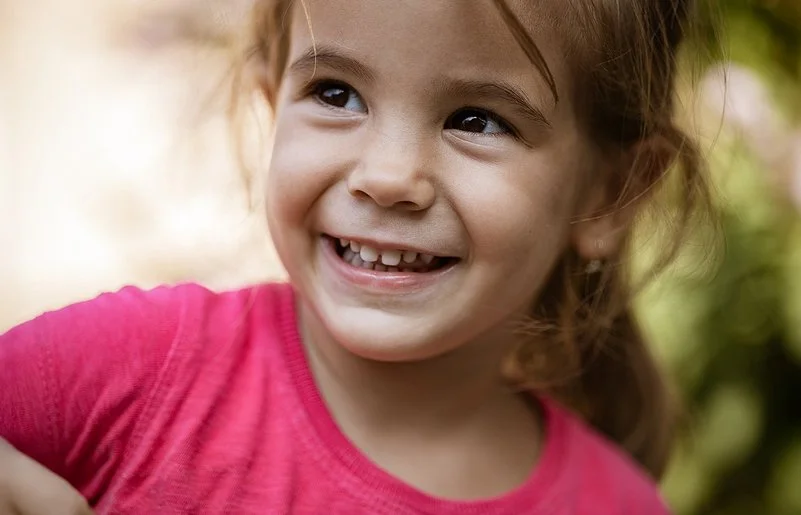 Ein ungefähr vierjähriges Mädchen schaut lächelnd zur Seite. Man sieht ihre gesunden Milchzähne.
