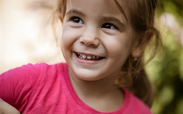 Ein ungefähr vierjähriges Mädchen schaut lächelnd zur Seite. Man sieht ihre gesunden Milchzähne.