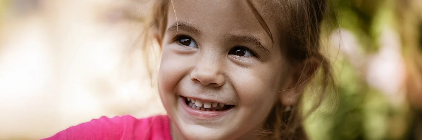 Ein ungefähr vierjähriges Mädchen schaut lächelnd zur Seite. Man sieht ihre gesunden Milchzähne.
