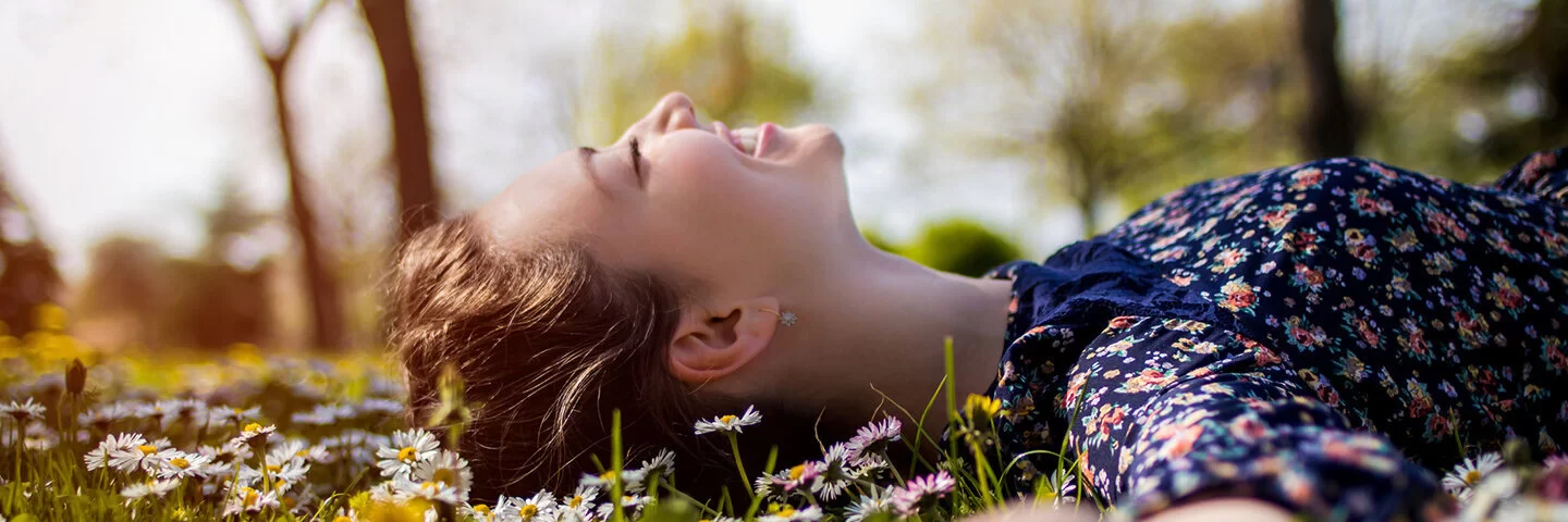 Eine junge Frau liegt lächelnd auf einer Wiese und hat die Augen geschlossen.