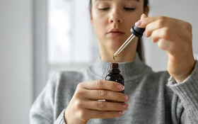 Junge Frau nimmt Algenöl-Tropfen mit einer Pipette aus einem Fläschchen.