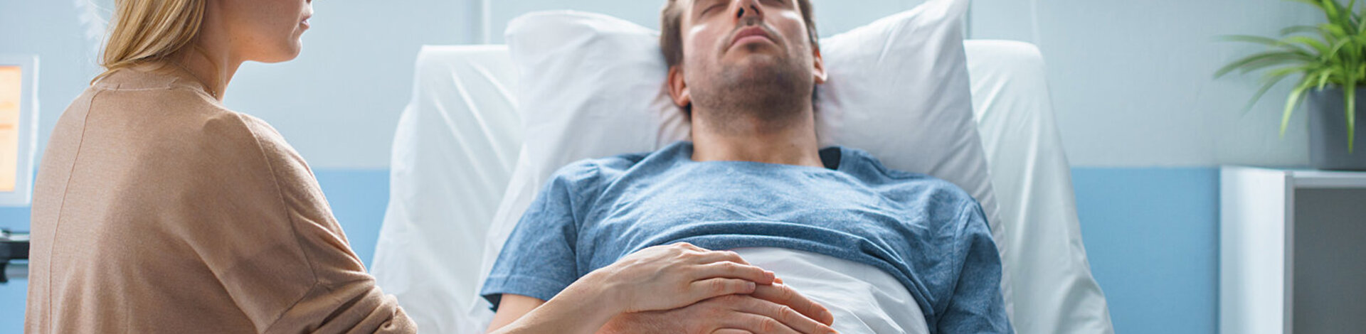 Ein Mann liegt im Krankenhaus; eine Frau hält seine Hand. Das Thema Organspende ist für Angehörige sehr herausfordernd.