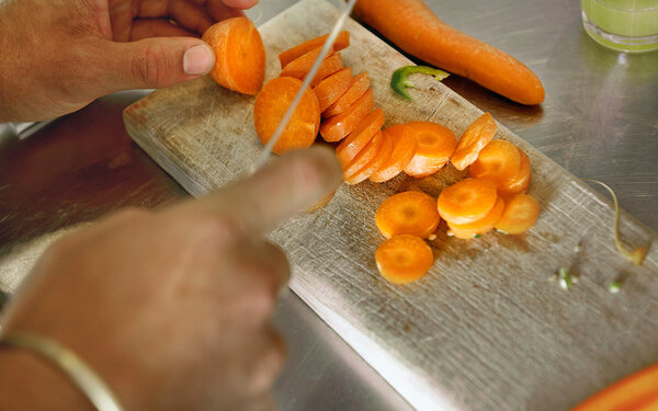 Person schneidet Karotten auf einem Holzbrett in Scheiben.