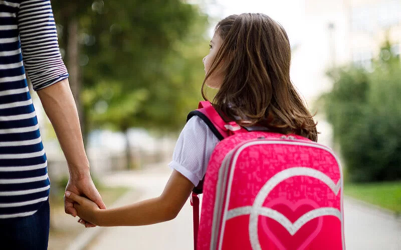Eine Mutter bringt ihre Tochter mit pinken Schulranzen auf dem Rücken zur Schule.